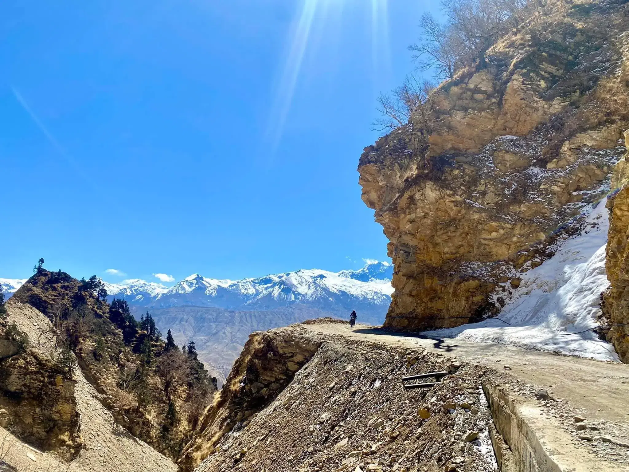 Mountain landscape featuring snowy terrain, water, a built structure, and blue sky.