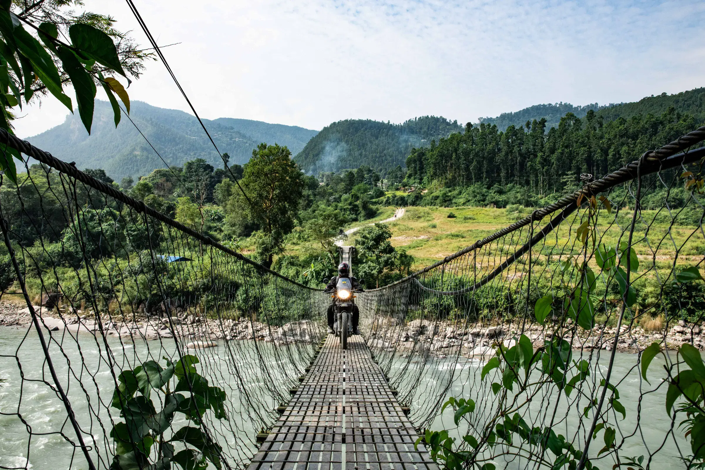 Outdoor scene featuring people, rocky terrain, a built structure, cloudy sky, and greenery.